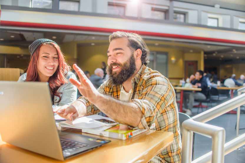 Estudiantes en campus con portatil hablando Residències per a estudiants de màsters i doctorats